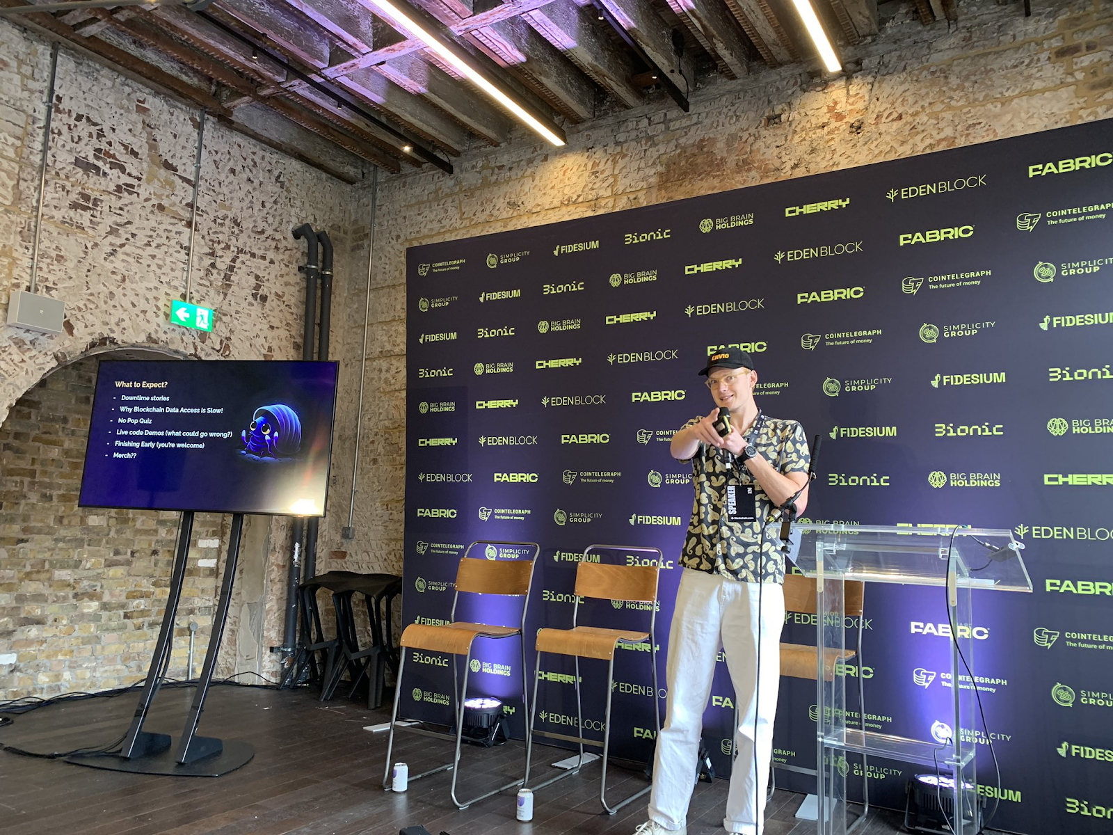 Speaker presenting onstage at Zebu Live in front of a sponsor backdrop with Fabric, Eden Block, Bionic, Cherry, Fidesium logos